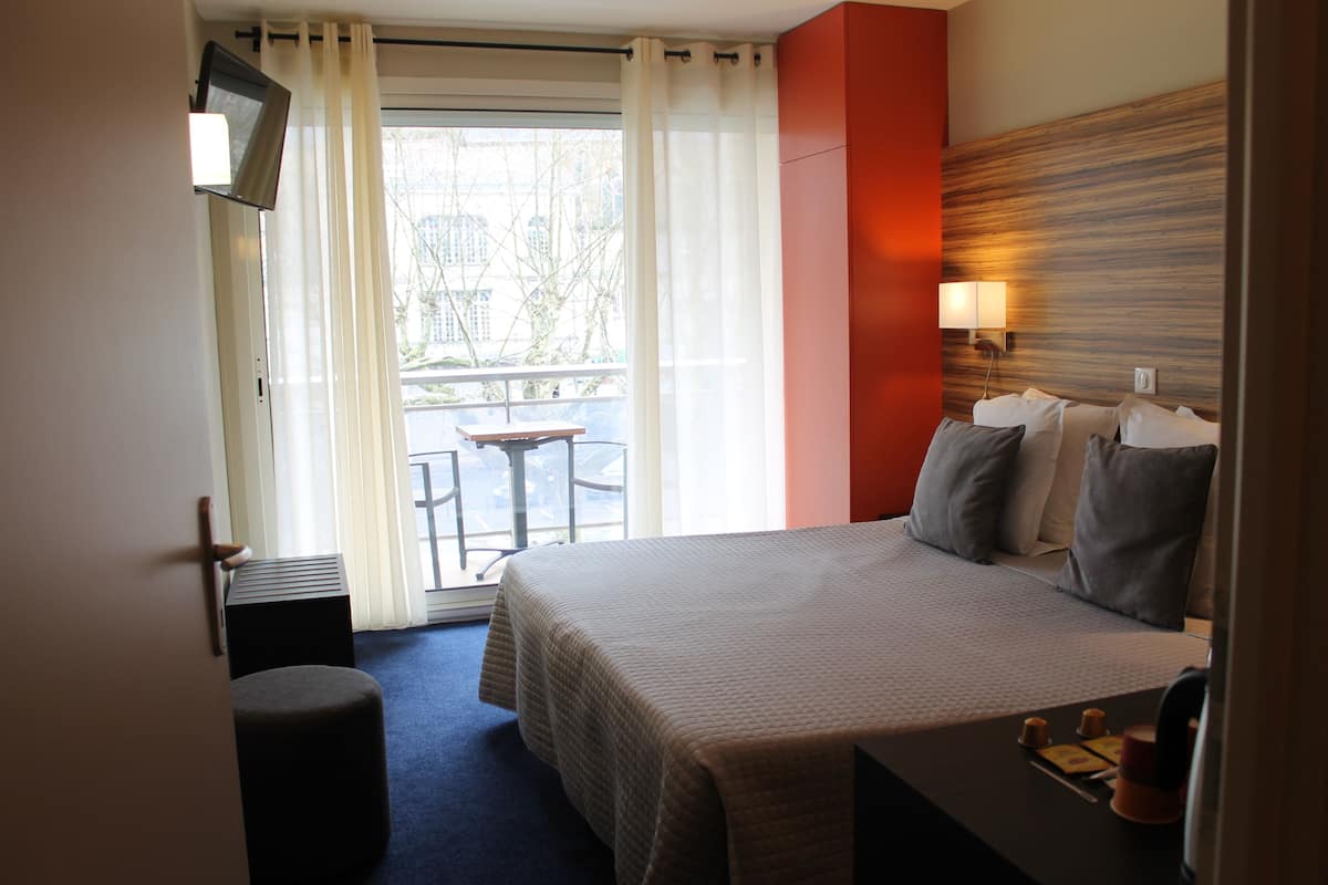 Ein Hotelzimmer mit Bett, Schreibtisch, Stuhl, Fernseher und Blick ins Freie.