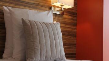 A bed with two pillows and a wall-mounted lamp.