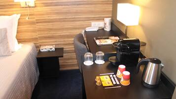 A hotel room with a bed, a desk with a coffee maker, cups, and a kettle.
