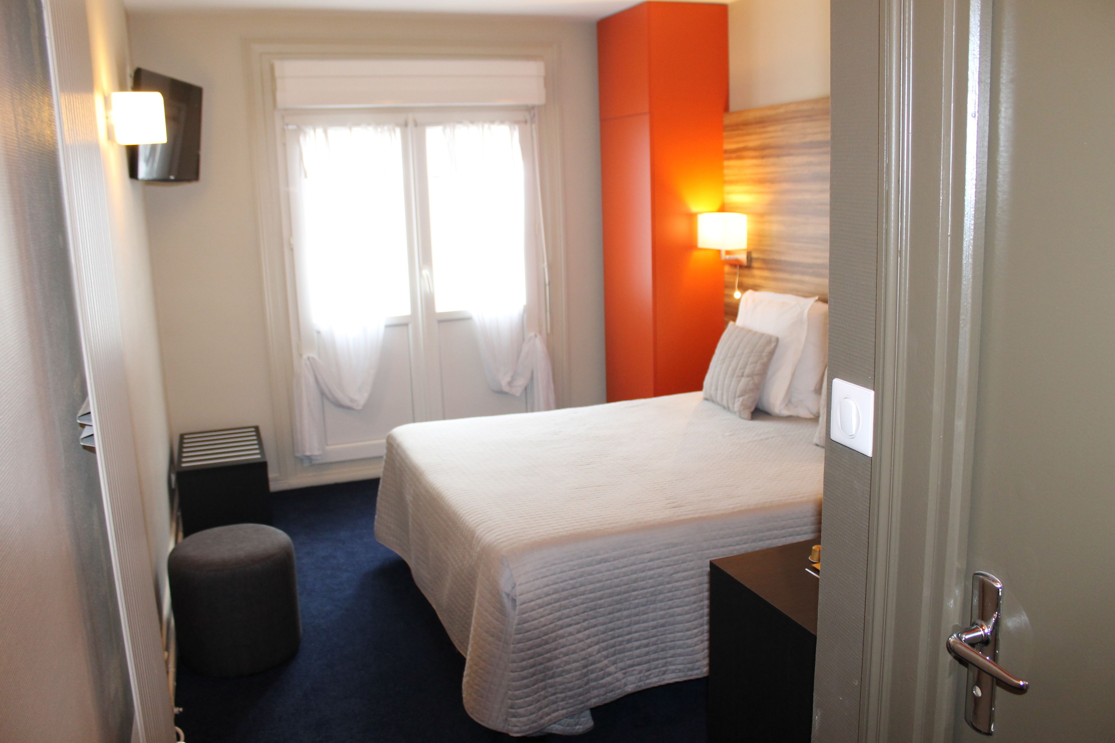 Habitación de hotel con una cama grande, una mesita de noche, una lámpara, una ventana con cortinas y una puerta.