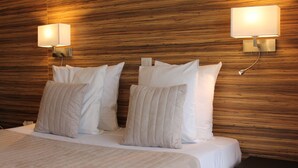 Hotellihuone, jossa on puinen sängynpääty, kaksi yöpöytävalaisinta ja siististi pedattu sänky, jossa on valkoiset lakanat ja useita tyynyjä.