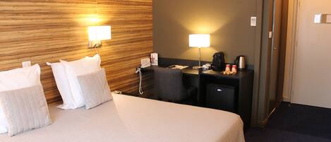 A hotel room with a large bed, two bedside lamps, a desk with a coffee maker, and a telephone.