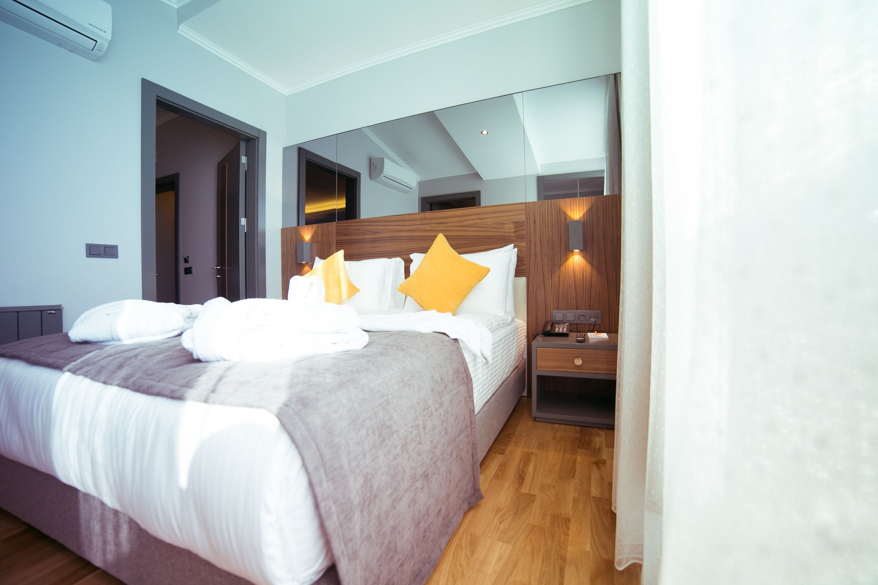 Una habitación de hotel moderna con una cama grande, una mesita de noche, un espejo y un cabecero de madera.