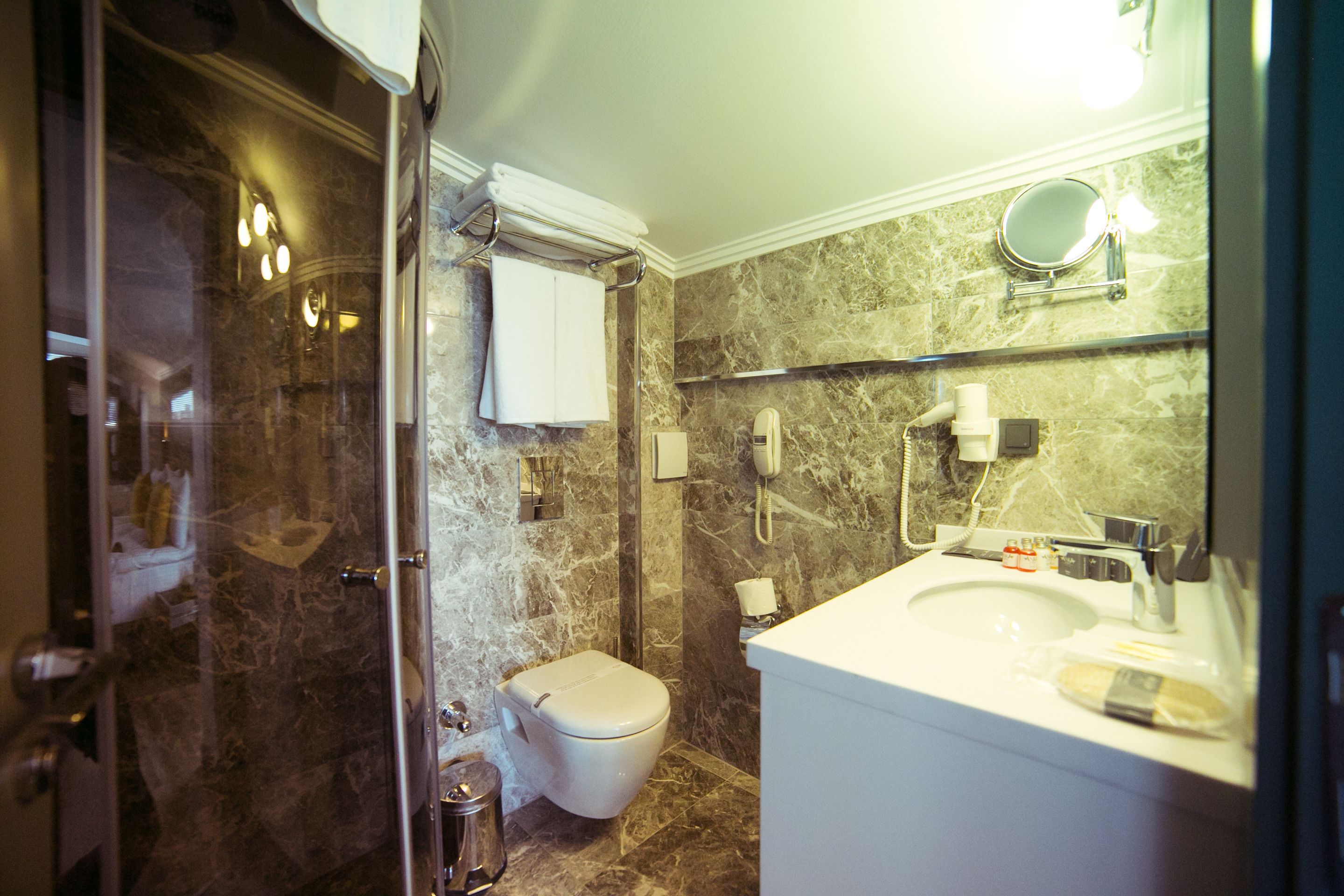 Un baño con cabina de ducha de vidrio, inodoro, lavabo con espejo y perchero para toallas.