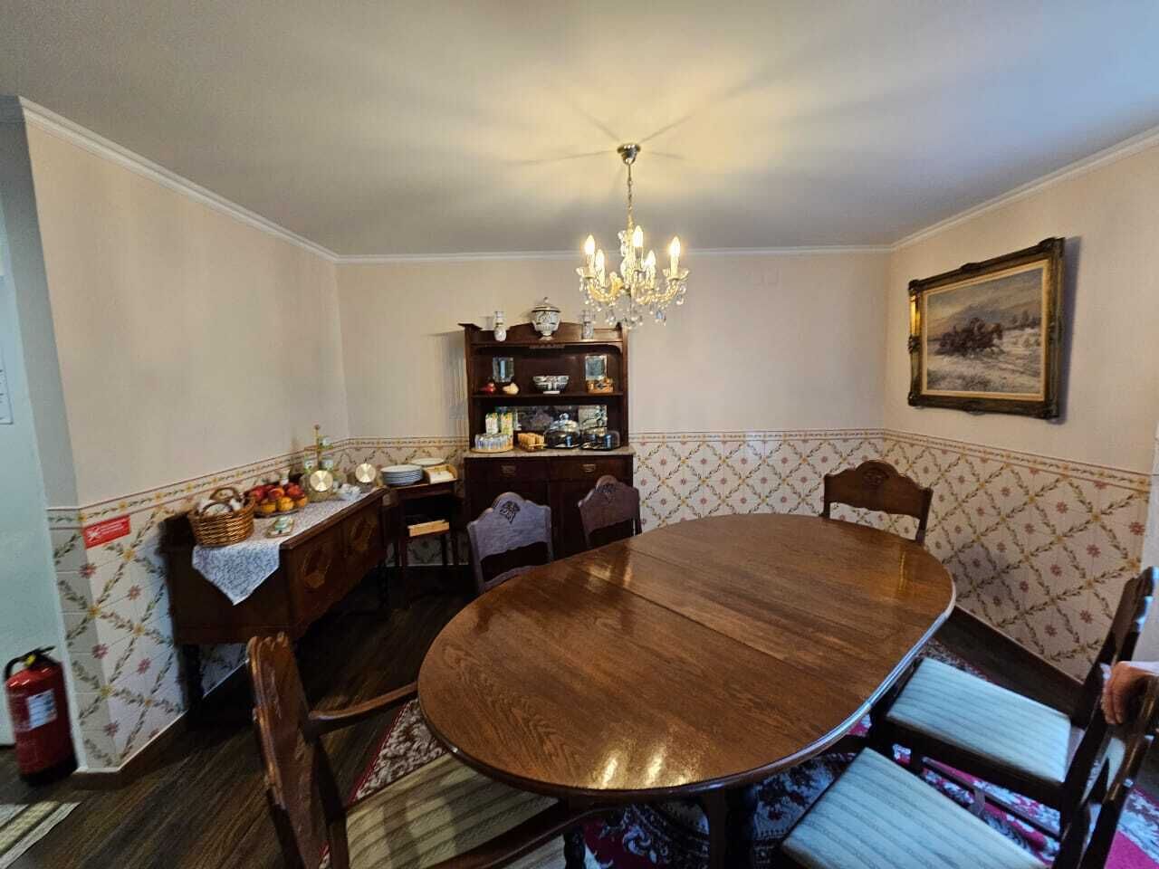 A dining room with a round wooden table, chairs, a chandelier, a buffet table, and a painting on the wall.
