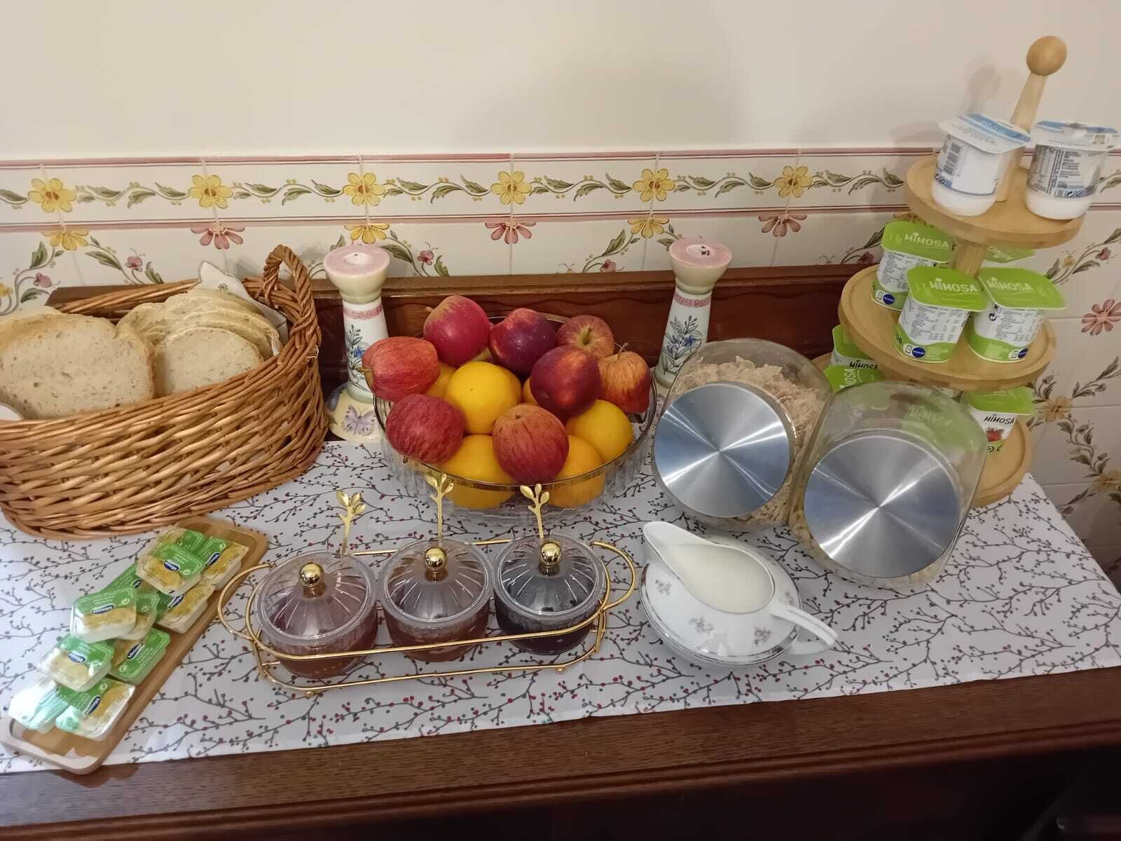 A kitchen counter with a fruit bowl, jars of preserves, a bread basket, and a milk jug.