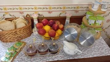 A kitchen counter with a fruit bowl, jars of preserves, a bread basket, and a milk jug.