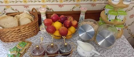 A kitchen counter with a fruit bowl, jars of preserves, a bread basket, and a milk jug.