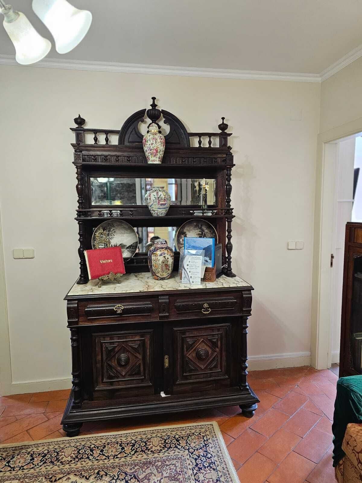 Un mueble de madera oscura con varios estantes, un espejo y objetos decorativos, incluyendo jarrones y una caja roja con la etiqueta 'Visitors'.