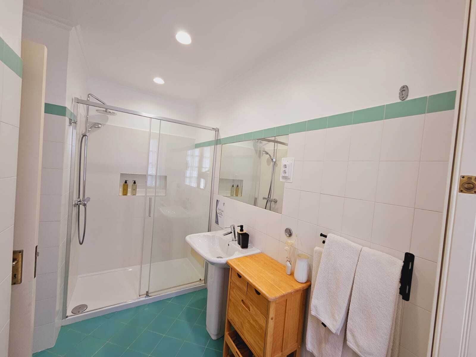 Un baño moderno con ducha de vidrio, lavamanos con tocador de madera y un espejo.
