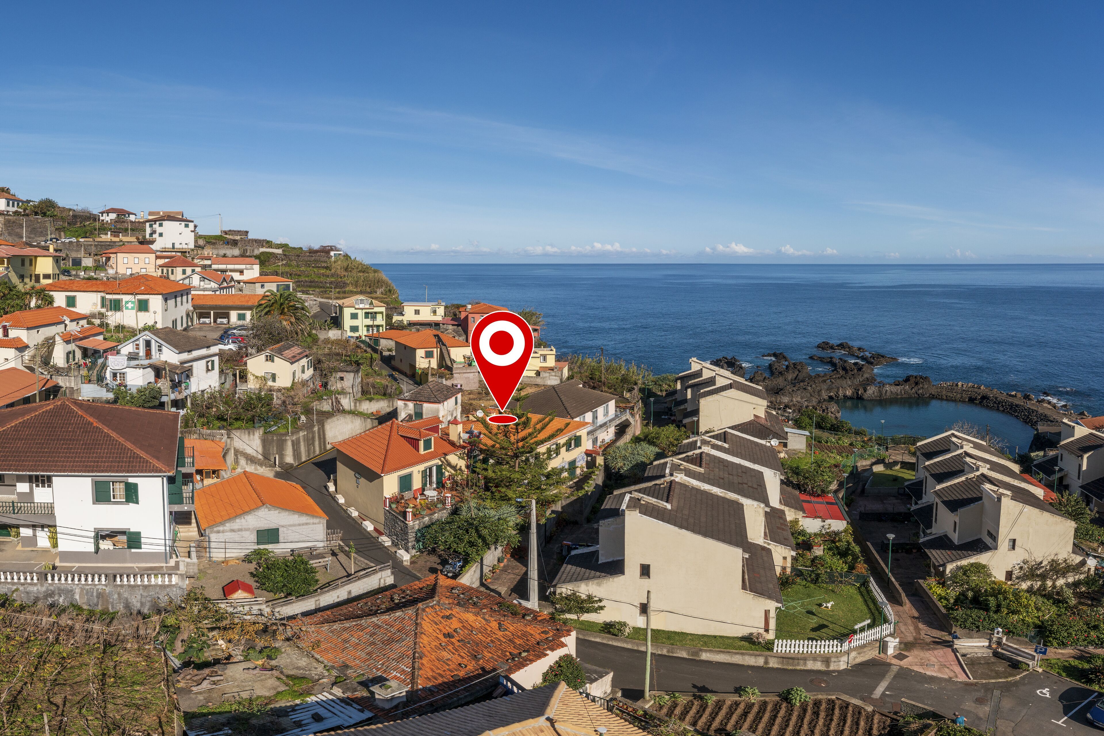 A coastal residential area with houses, a clear view of the sea, and a red location marker.