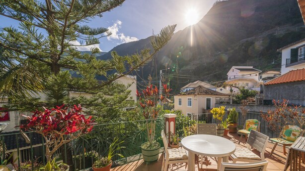 A patio with a round table and chairs, surrounded by potted plants and a view of a mountain. - Casa das Videiras (Porto Moniz)