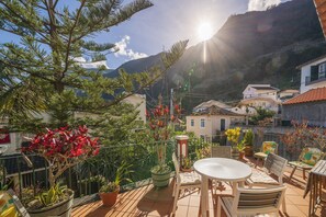 A patio with a round table and chairs, surrounded by potted plants and a view of a mountain. - Casa das Videiras (Porto Moniz)