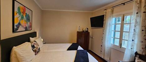 A hotel room with two beds, a flat-screen TV, a wooden cabinet, and a window with curtains.
