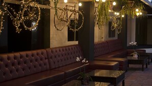 A modern lounge area with leather sofas and tables, decorative bicycles, hanging plants, and ambient lighting. - Pachamama - Hotel - Hostel (Managua)