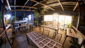 An outdoor patio area with hexagonal tiles, tables, chairs, hanging plants, and a view of a building in the background. - Pachamama - Hotel - Hostel (Managua)