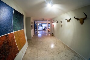 Un couloir doté d’un sol carrelé, une grande peinture abstraite sur le mur de gauche et plusieurs crânes d’animaux fixés au mur de droite.