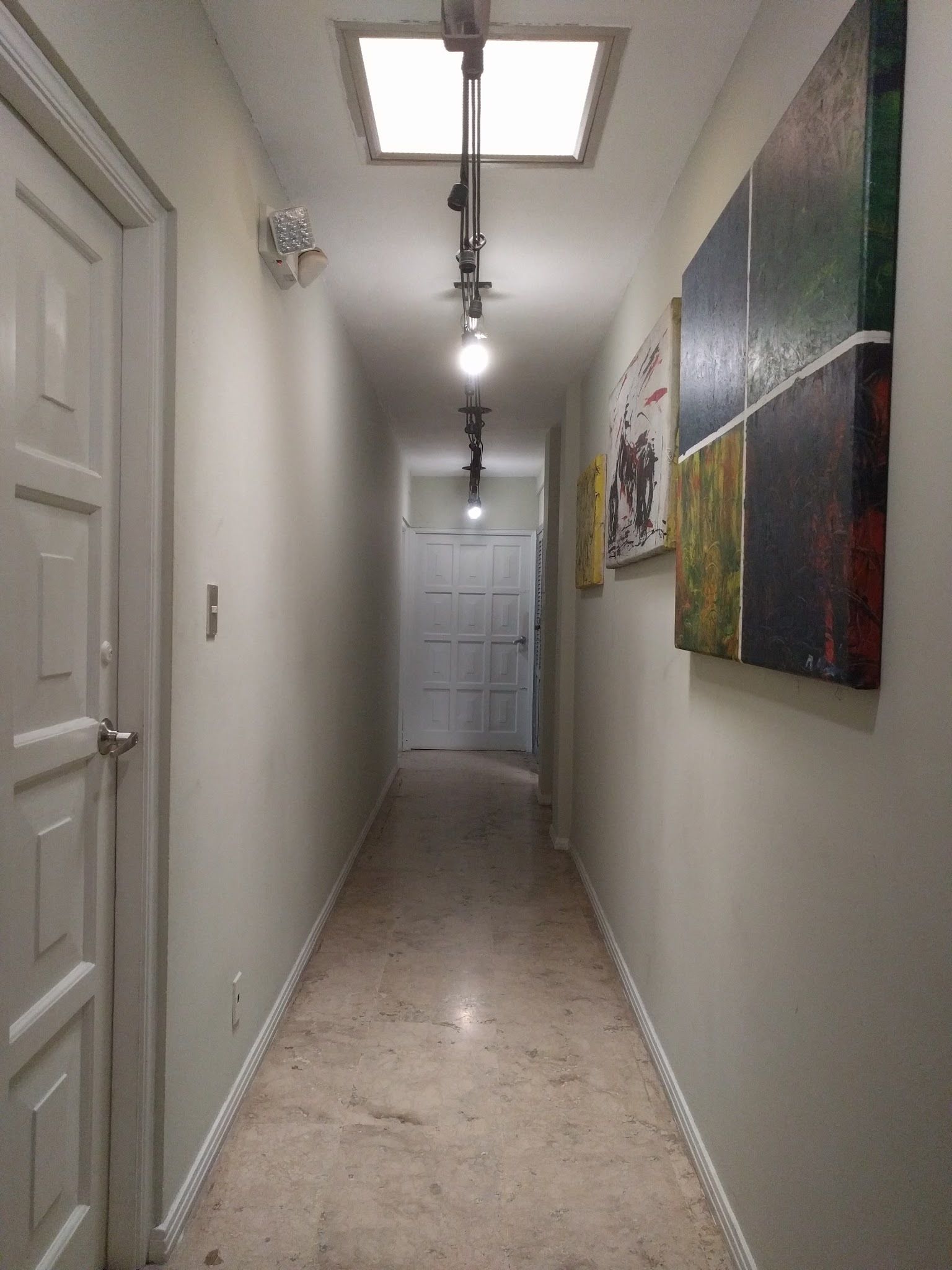 A narrow hallway with a ceiling light, a door on the left, and a door at the end.