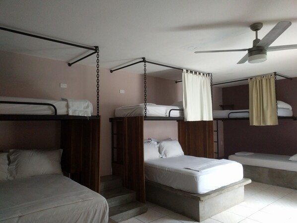 A dormitory room with bunk beds, a ceiling fan, and a staircase.