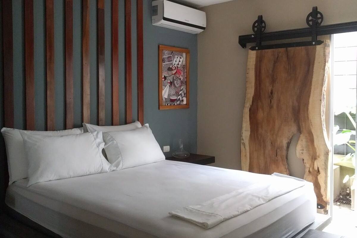 A bed with white bedding, a wooden headboard, a ceiling fan, and a window with a curtain.