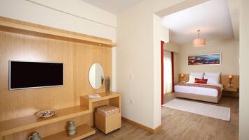 A modern hotel room with a flat-screen TV, wooden shelving, a bedside table with a vase, a bed with white bedding, and a painting on the wall.