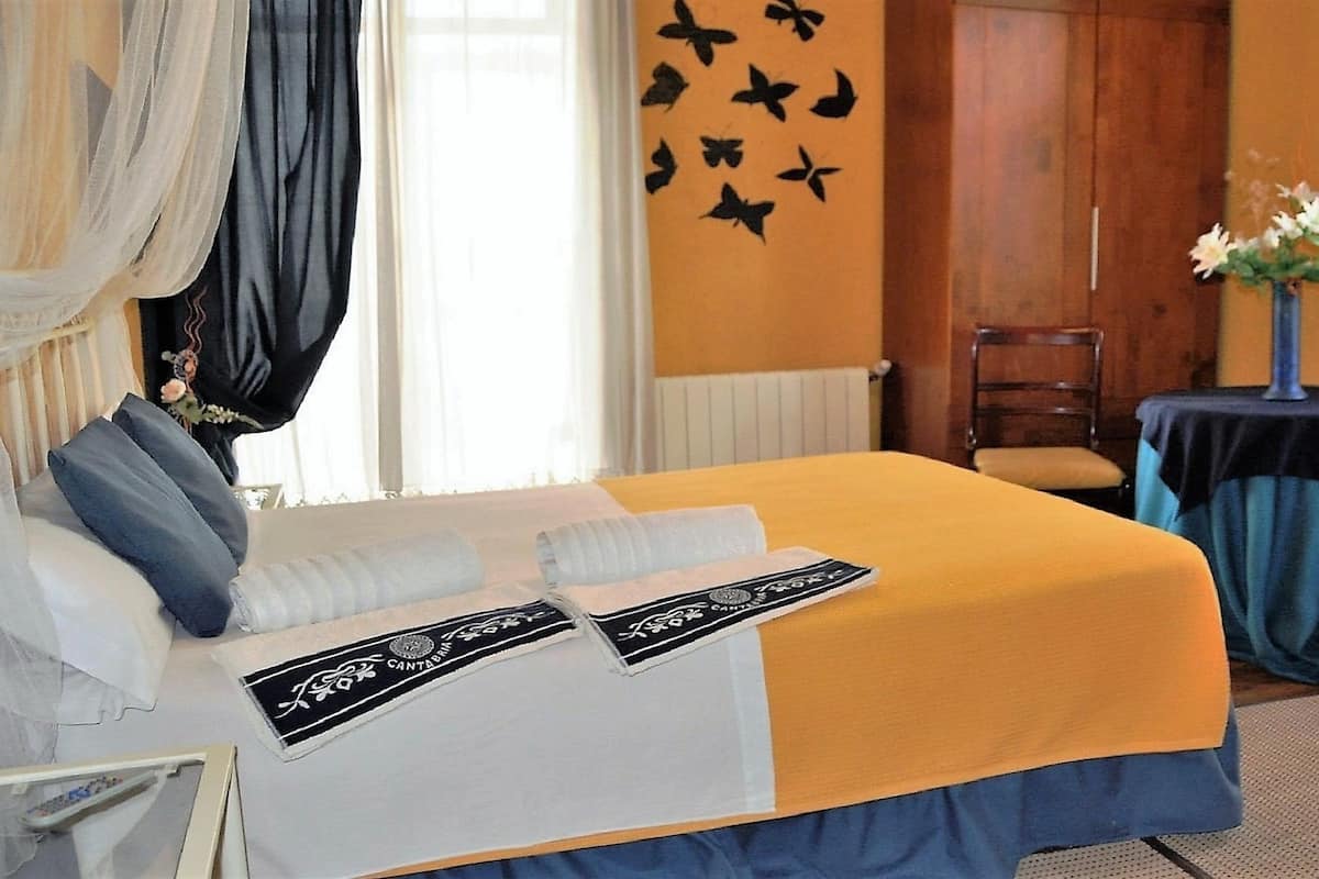 Habitación de hotel con cama, una silla, una mesita con un jarrón de flores y una pared decorada con una mariposa.