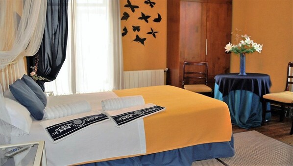 A hotel room with a bed, a chair, a small table with a vase of flowers, and a wall with a butterfly decoration. - Hospedaje Botín (Santander)