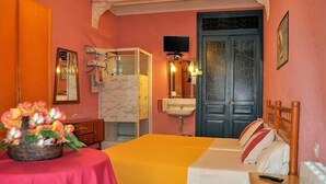 A room with a bed, a table with a vase of flowers, a sink, and a television. - Hospedaje Botín (Santander)