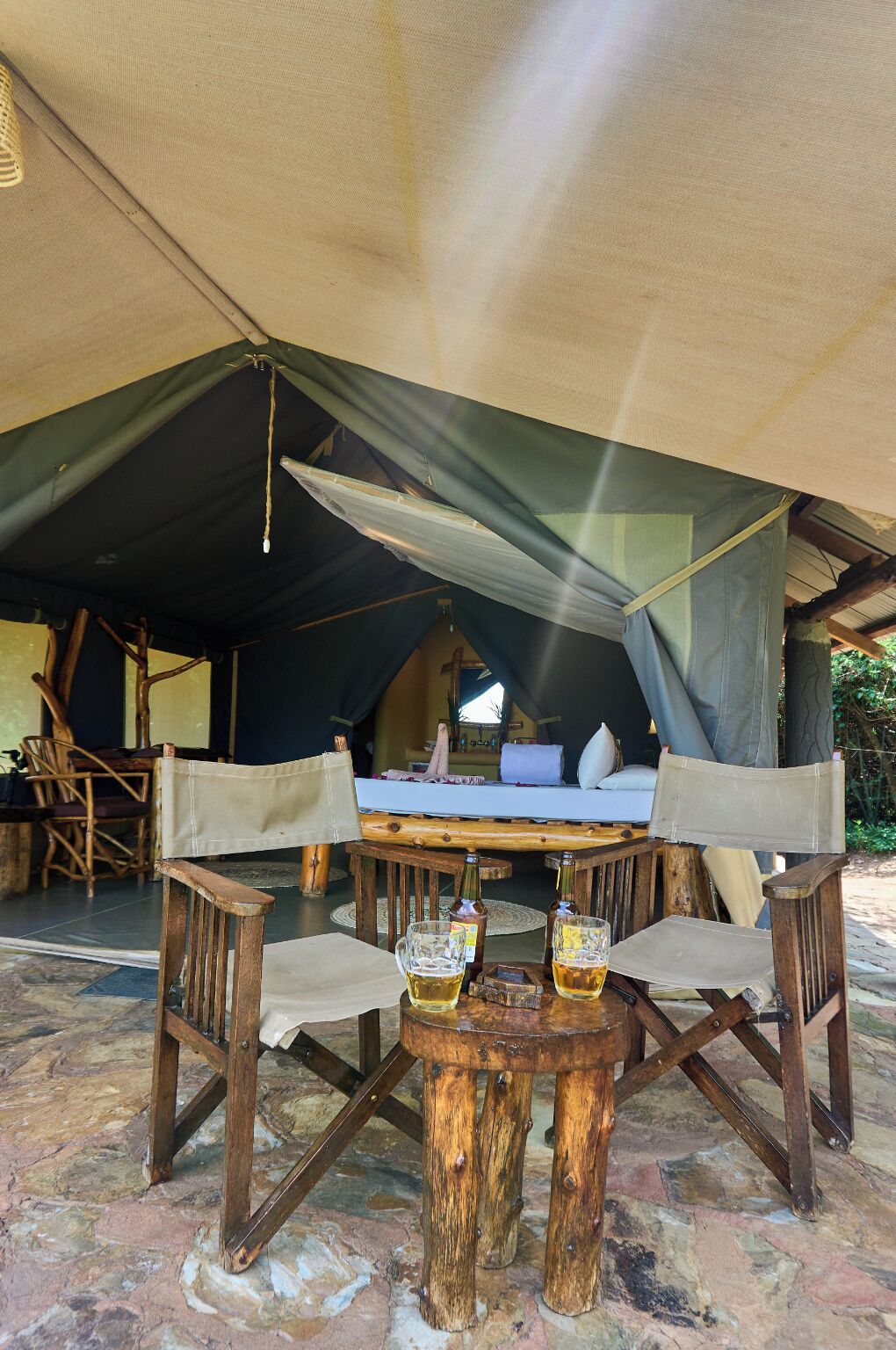 A tent with a bed, two chairs, and a table with two glasses of beer.