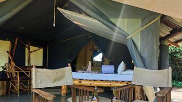 A tent with a bed, two chairs, and a table with two glasses of beer.