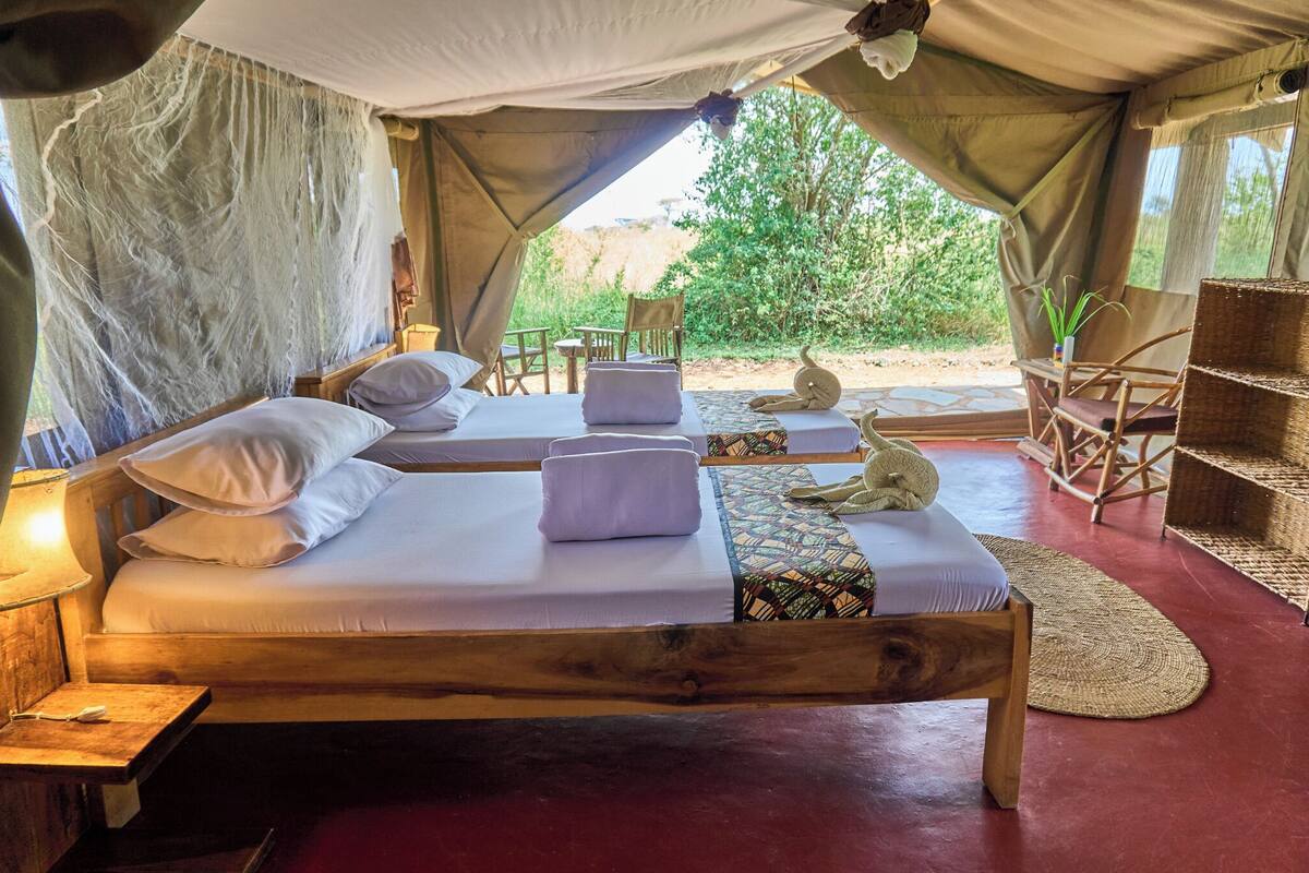 A tented accommodation with two beds, a table, chairs, and a view of the outdoors.