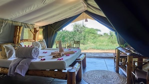 A tented accommodation with a bed, pillows, a towel, and a view of greenery. - Ikoma tented Camp (Serengeti)