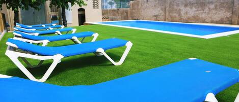 A pool area with artificial grass and blue lounge chairs.