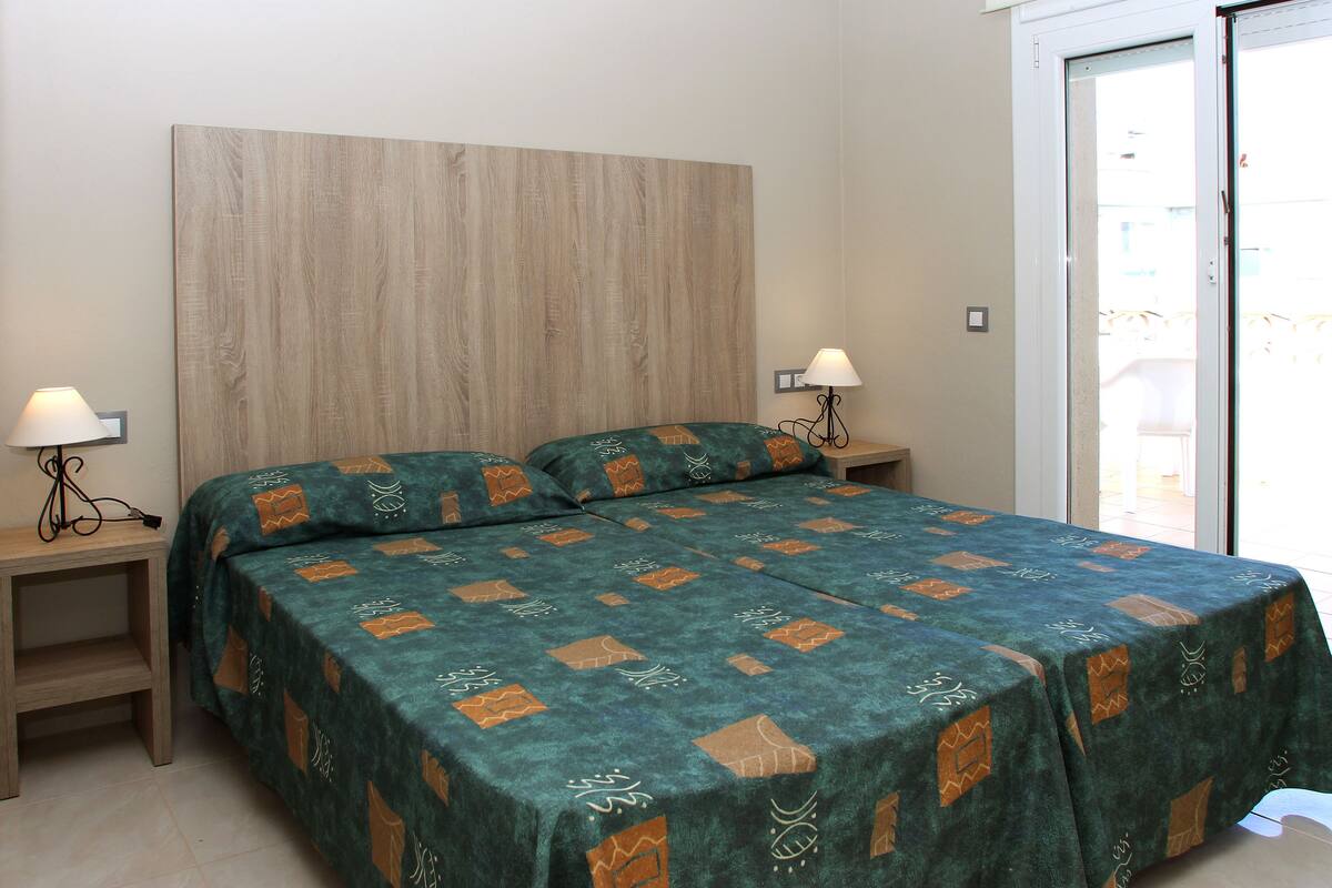 A double bed with a patterned bedspread, two bedside tables with lamps, and a wooden headboard.
