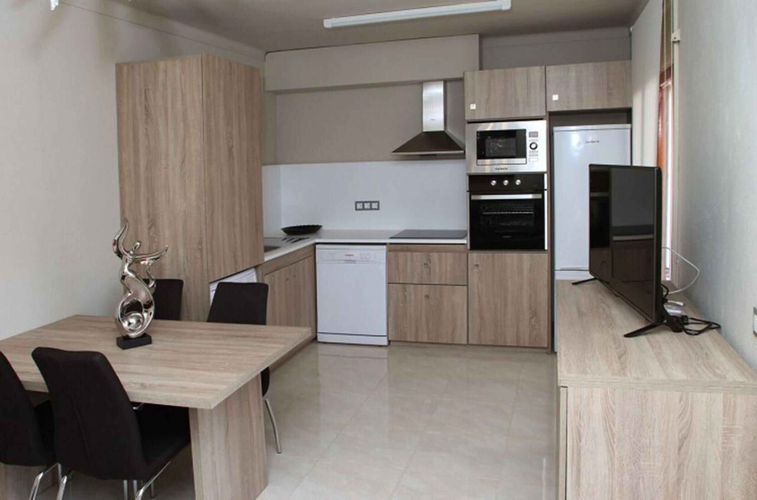 A modern kitchen with a built-in oven, microwave, and refrigerator. There is a dining area with a table and chairs.