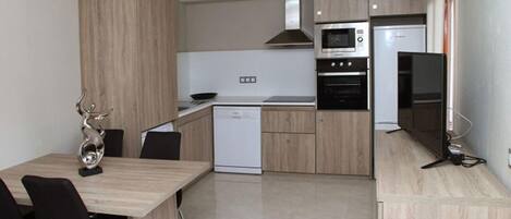 A modern kitchen with a built-in oven, microwave, and refrigerator. There is a dining area with a table and chairs.