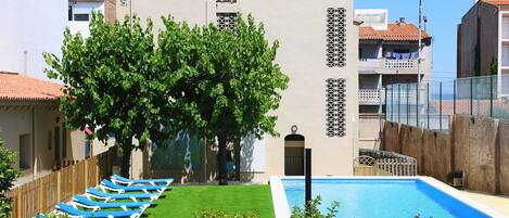 A modern building with a swimming pool, green lawn, and lounge chairs.