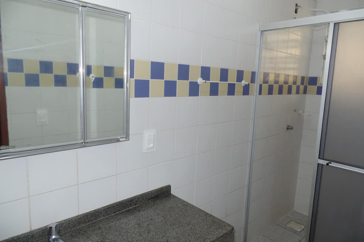 Ein Badezimmer mit weißen Fliesen, einer Granit-Arbeitsplatte, einer Glasdusche und einem Spiegel mit Chromrahmen.