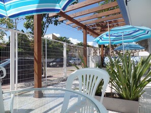 A patio area with a round table, white chairs, and blue-striped umbrellas. - Residencial Valparaíso (Florianópolis)