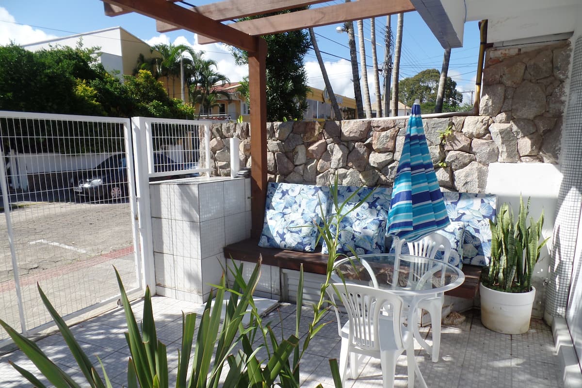 Eine Terrasse im Freien mit einer Steinmauer, einem weißen Metallgitter, einem Tisch mit Stühlen und Topfpflanzen.