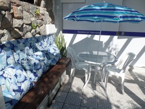 A seating area with a blue floral sofa, a round glass table, and white plastic chairs. - Residencial Valparaíso (Florianópolis)