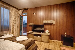 Quarto de hotel com paredes de painel de madeira, televisão, pequeno frigorífico e porta de vidro deslizante para uma varanda.