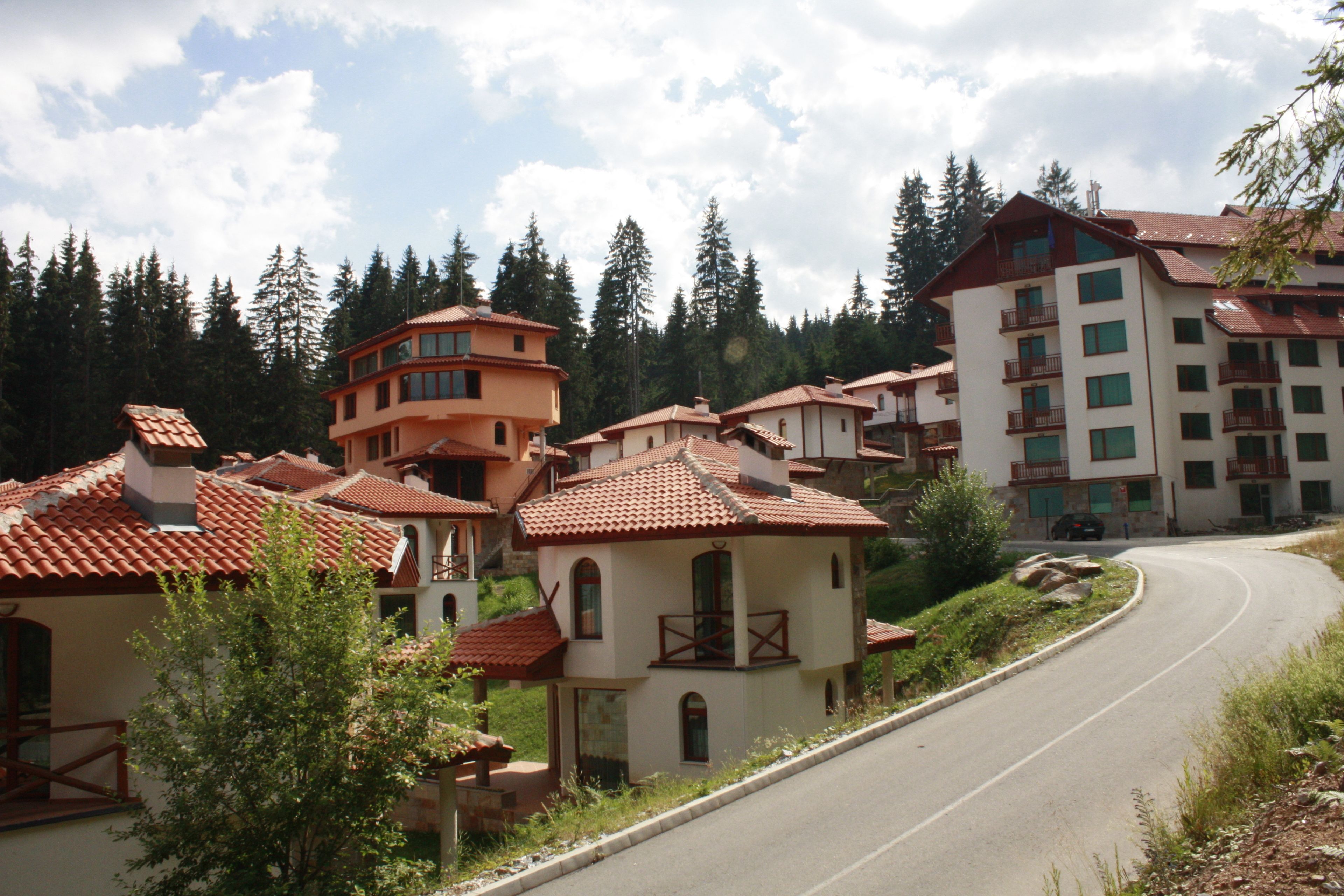 A residential area with multi-story buildings, a curved road, and surrounding greenery.