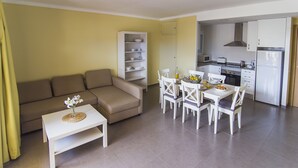 Un salon moderne comprenant un canapé, une table à manger et des chaises, une cuisine équipée et une bibliothèque.
