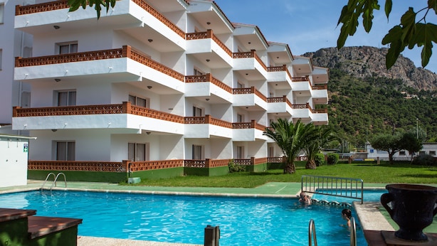 Un hôtel à plusieurs étages, doté de balcons, d’une piscine et surplombant un paysage montagneux.