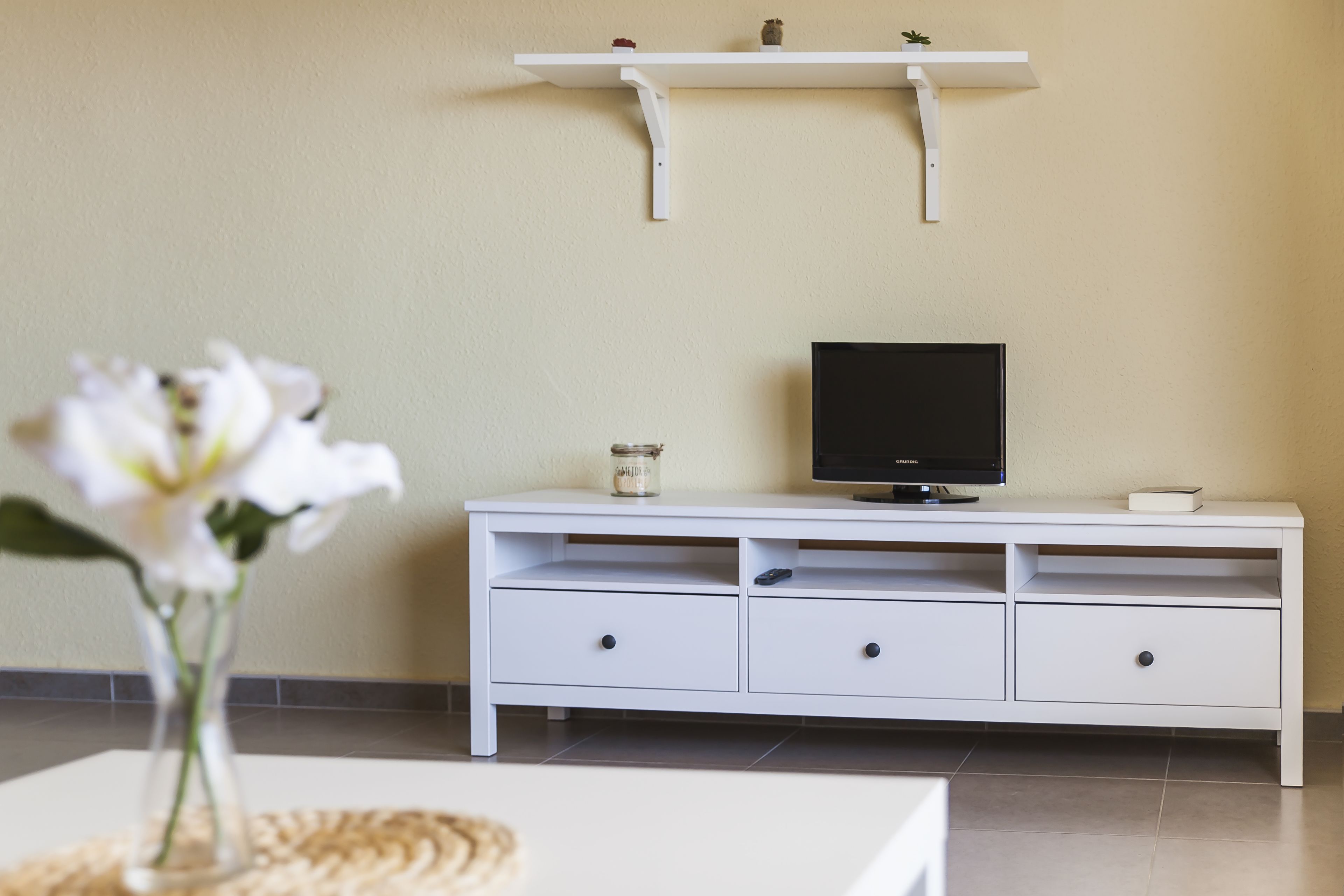 A white TV stand with a flat-screen TV, a small plant, and a candle.