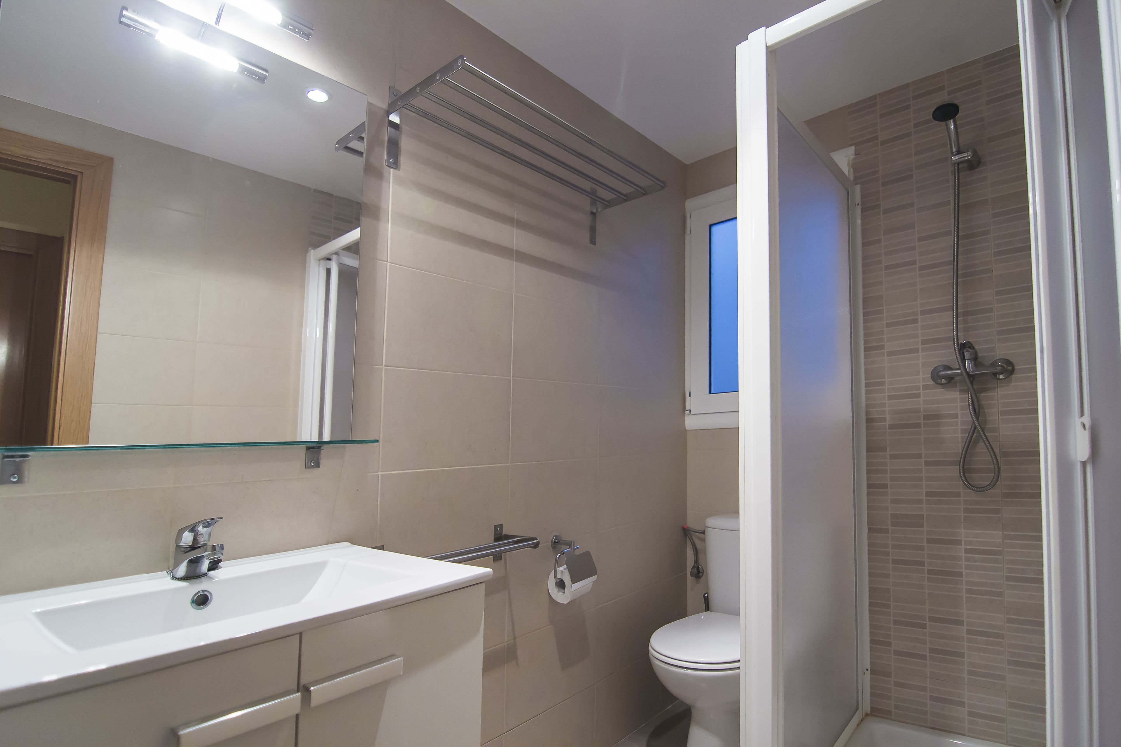 Un baño moderno con lavamanos, espejo y ducha blancos.