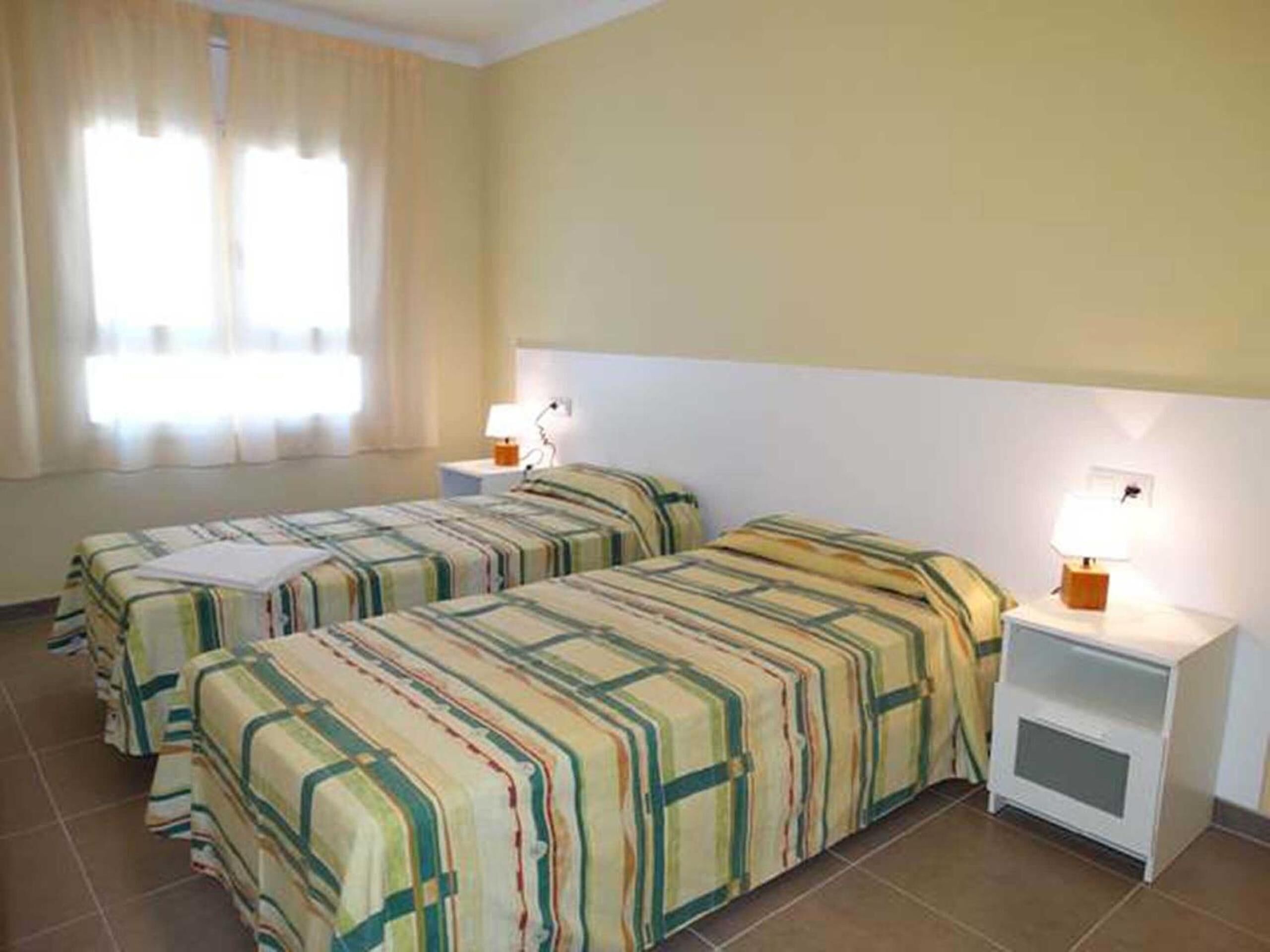 Una habitación de hotel con dos camas, una mesita de noche con lámpara y una ventana con cortinas.