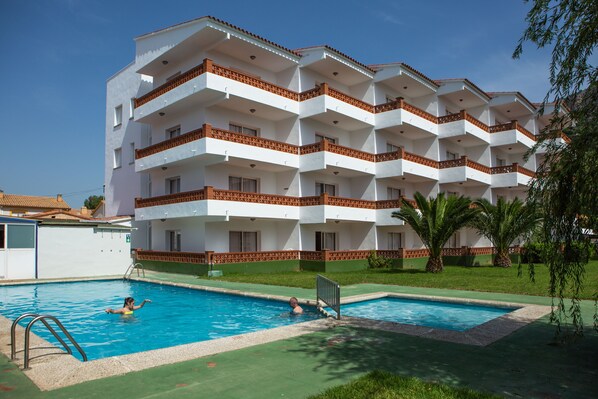 A multi-story hotel with a swimming pool, balconies, and a green lawn.