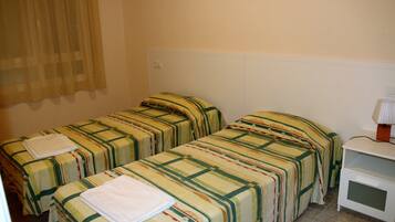 A hotel room with two single beds, each with a striped bedspread and a folded white towel. There is a small white nightstand with a lamp on it.